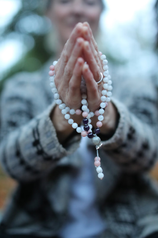 Picture of hands holding mala beads in prayer, outside in nature